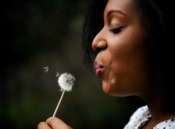 woman in white top blowing dandelion