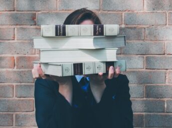 person holding pile of books near face